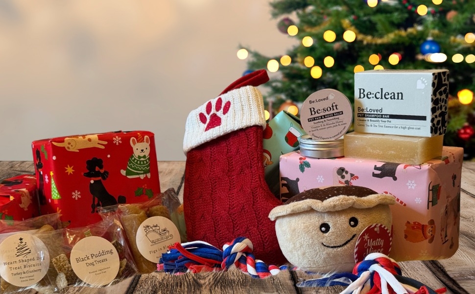 Assorted pet care products including a red stocking, soap bars, and a plush toy in front of a Christmas tree.