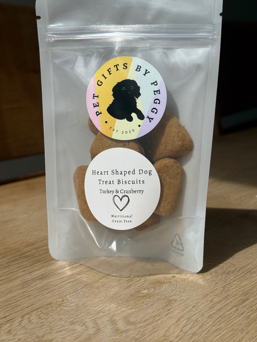 Package of heart-shaped dog treat biscuits with 'Pet Gifts by Peggy' label on a wooden surface.