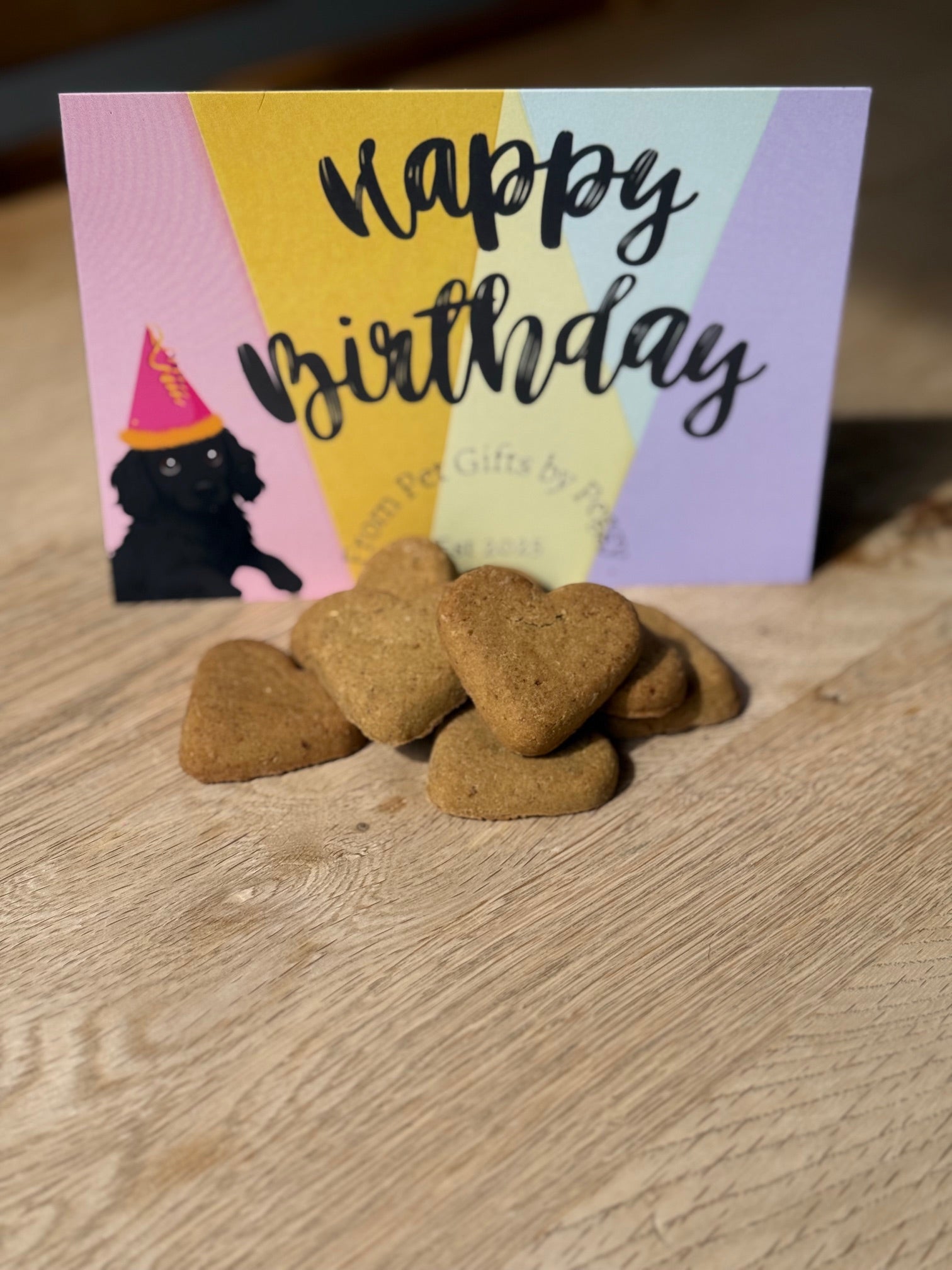 Dog treats in front of a 'Happy Birthday' card with a dog wearing a party hat on a wooden surface.