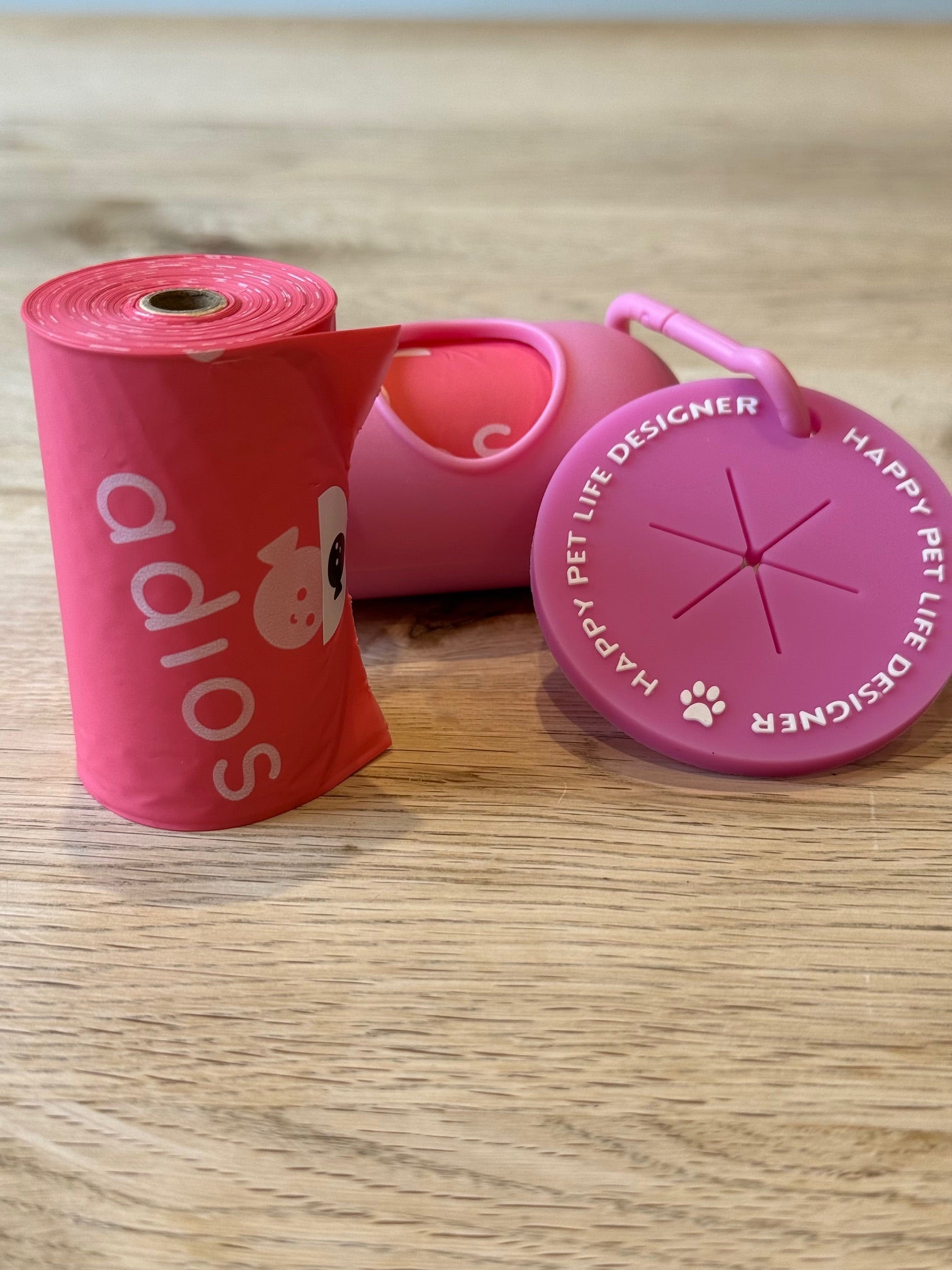 Pink pet waste bag dispenser with a roll of bags on a wooden surface