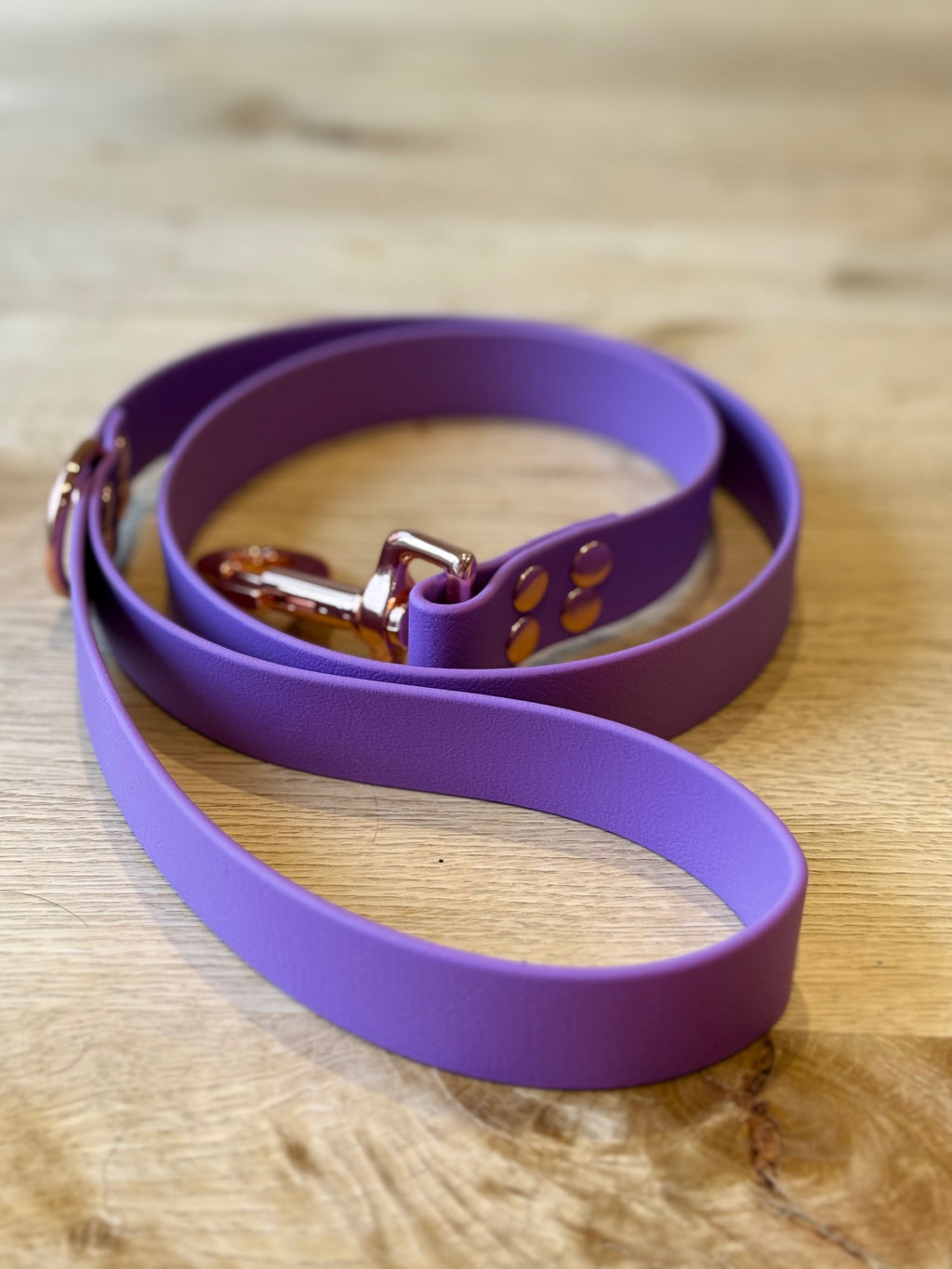 Purple dog leash with rose gold hardware on a wooden surface