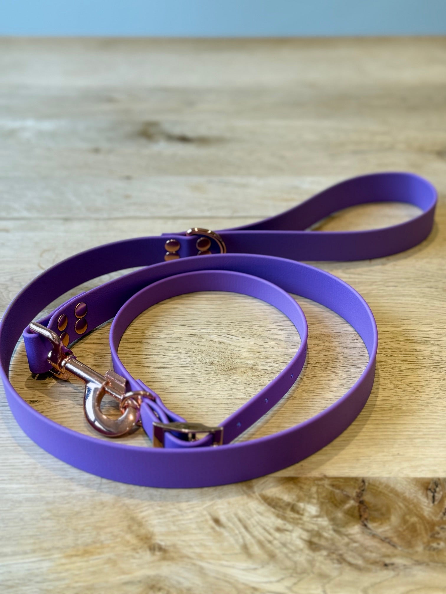 Purple dog leash with rose gold hardware on a wooden surface