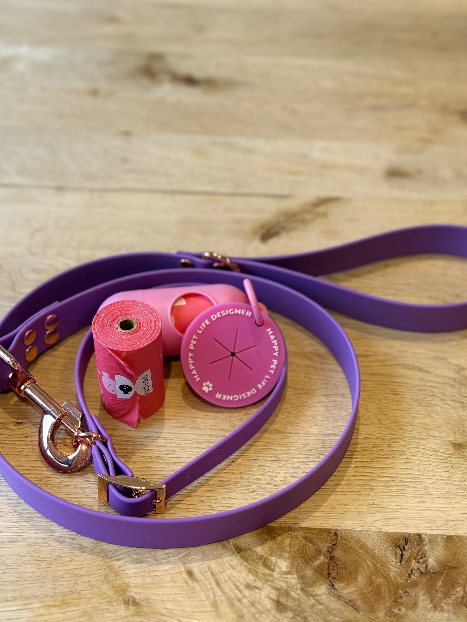Purple dog leash with pink bag and clip on a wooden surface