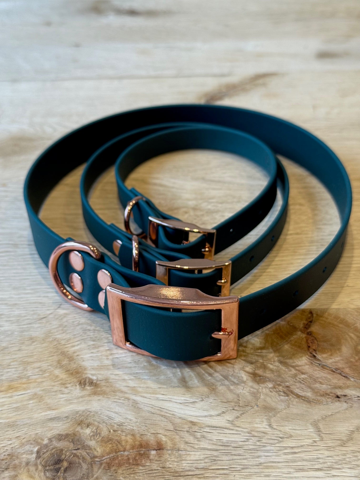 Two green leather dog collars with rose gold buckles on a wooden surface