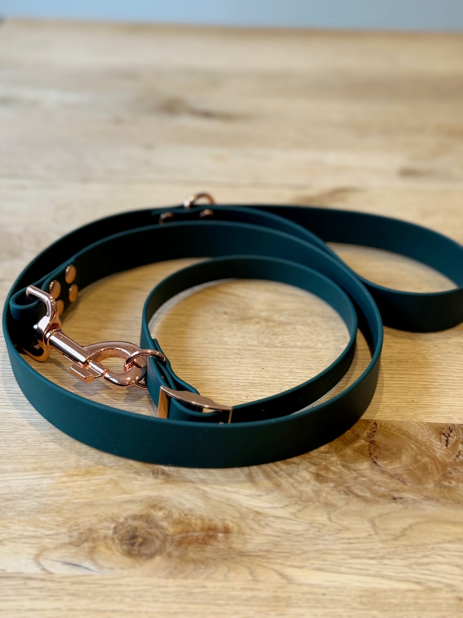Green dog leash with rose gold clasp on a wooden surface