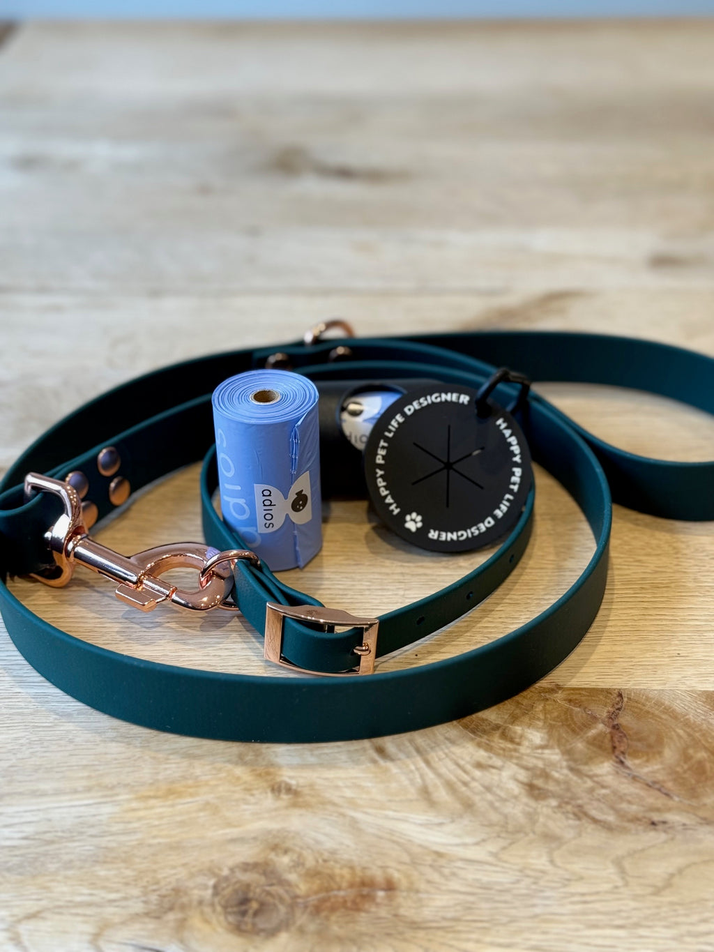 Green leather dog leash with rose gold hardware on a wooden surface