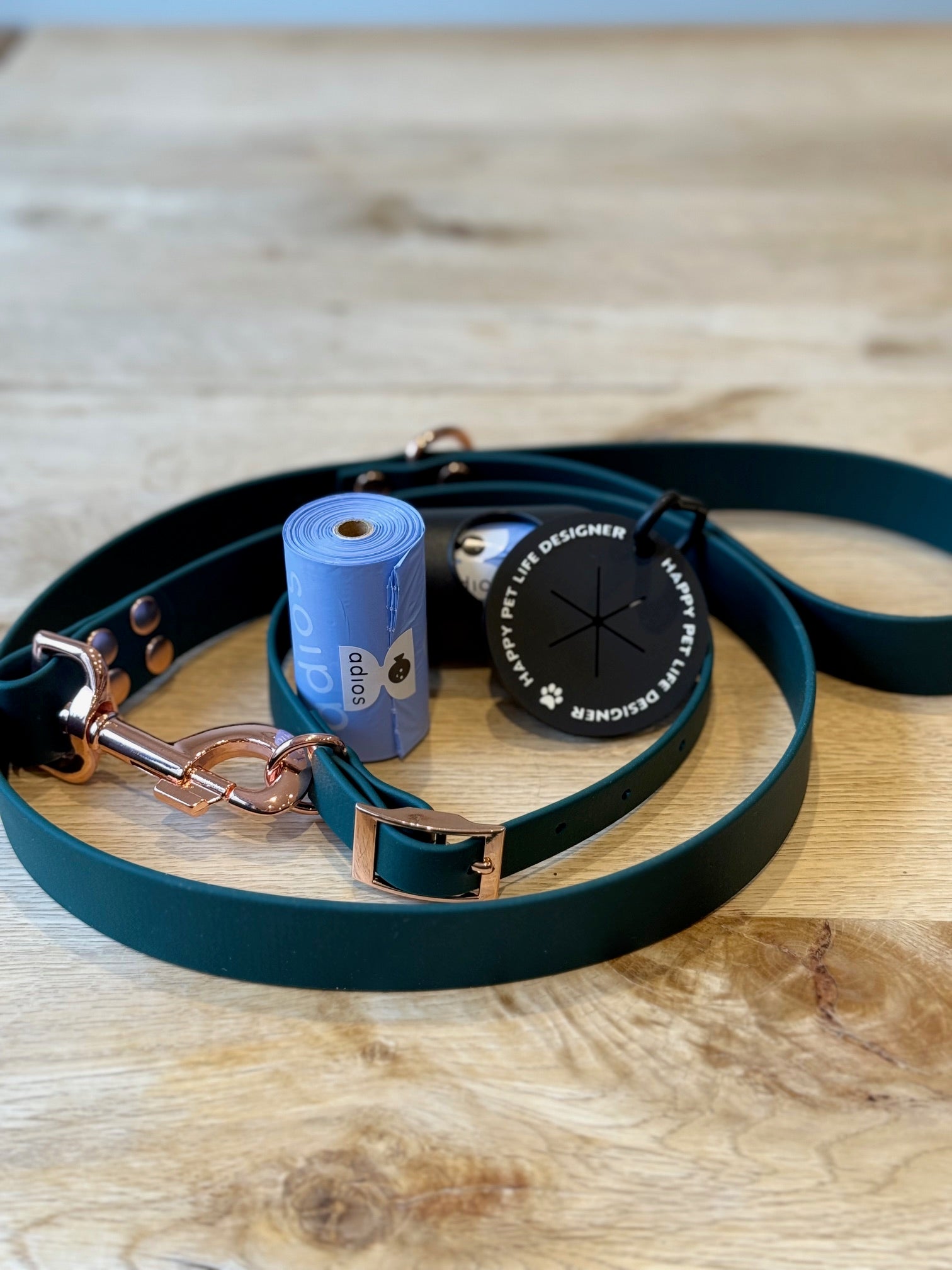 Green leather dog leash with rose gold hardware on a wooden surface