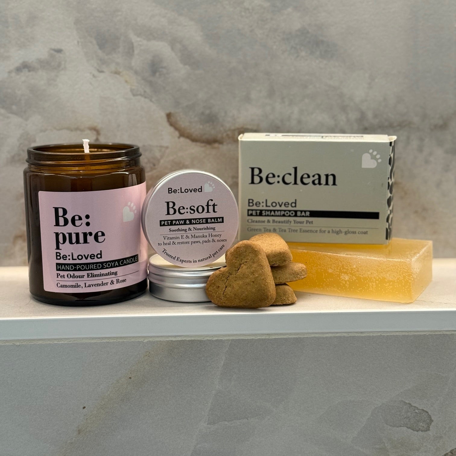 Pet care products including a candle, shampoo bar, and soap on a stone surface.