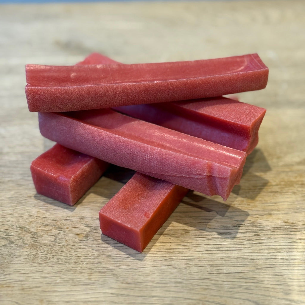 Stack of pink dog yak chews on a wooden surface with a blue background