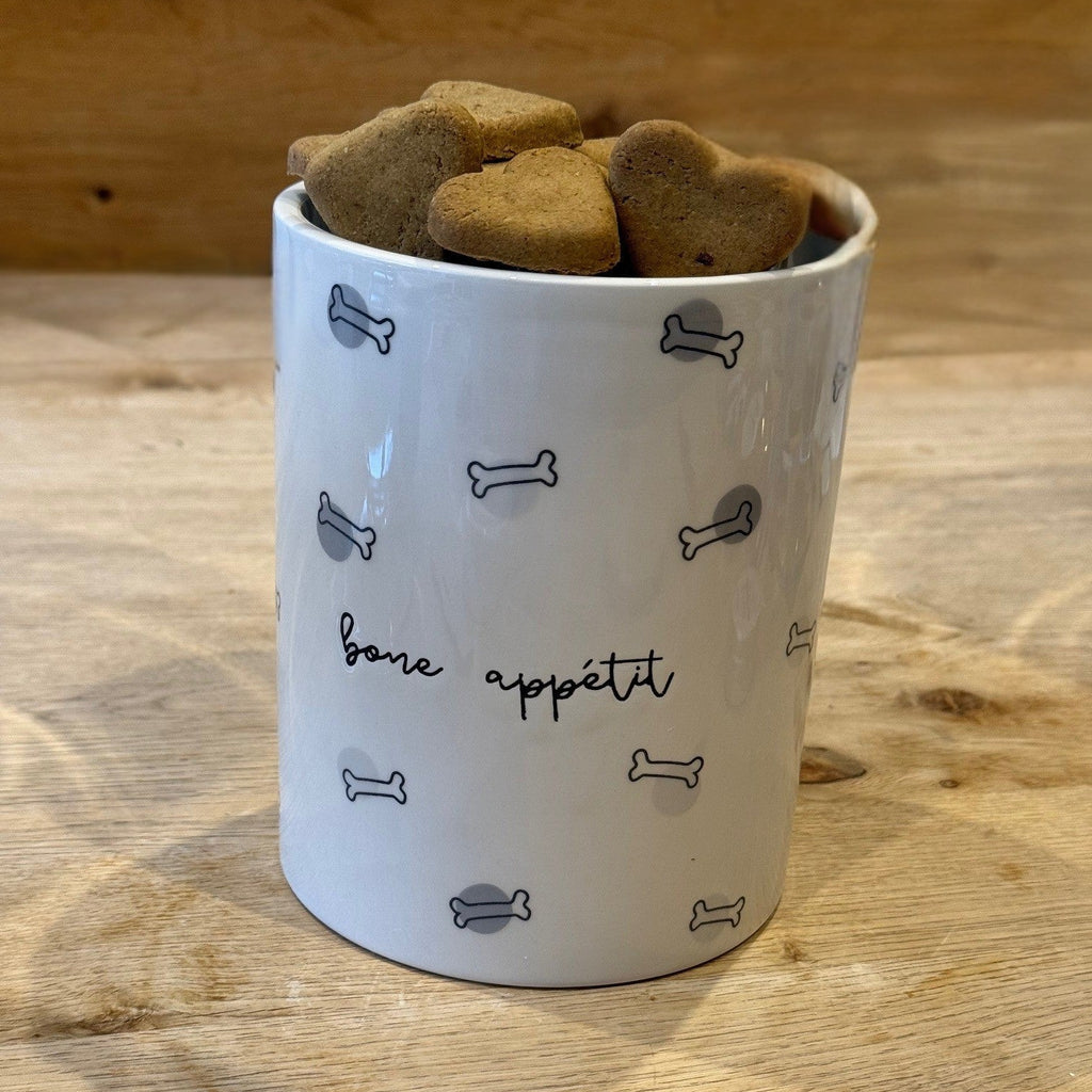 White container with dog treats shaped like bones on a wooden surface