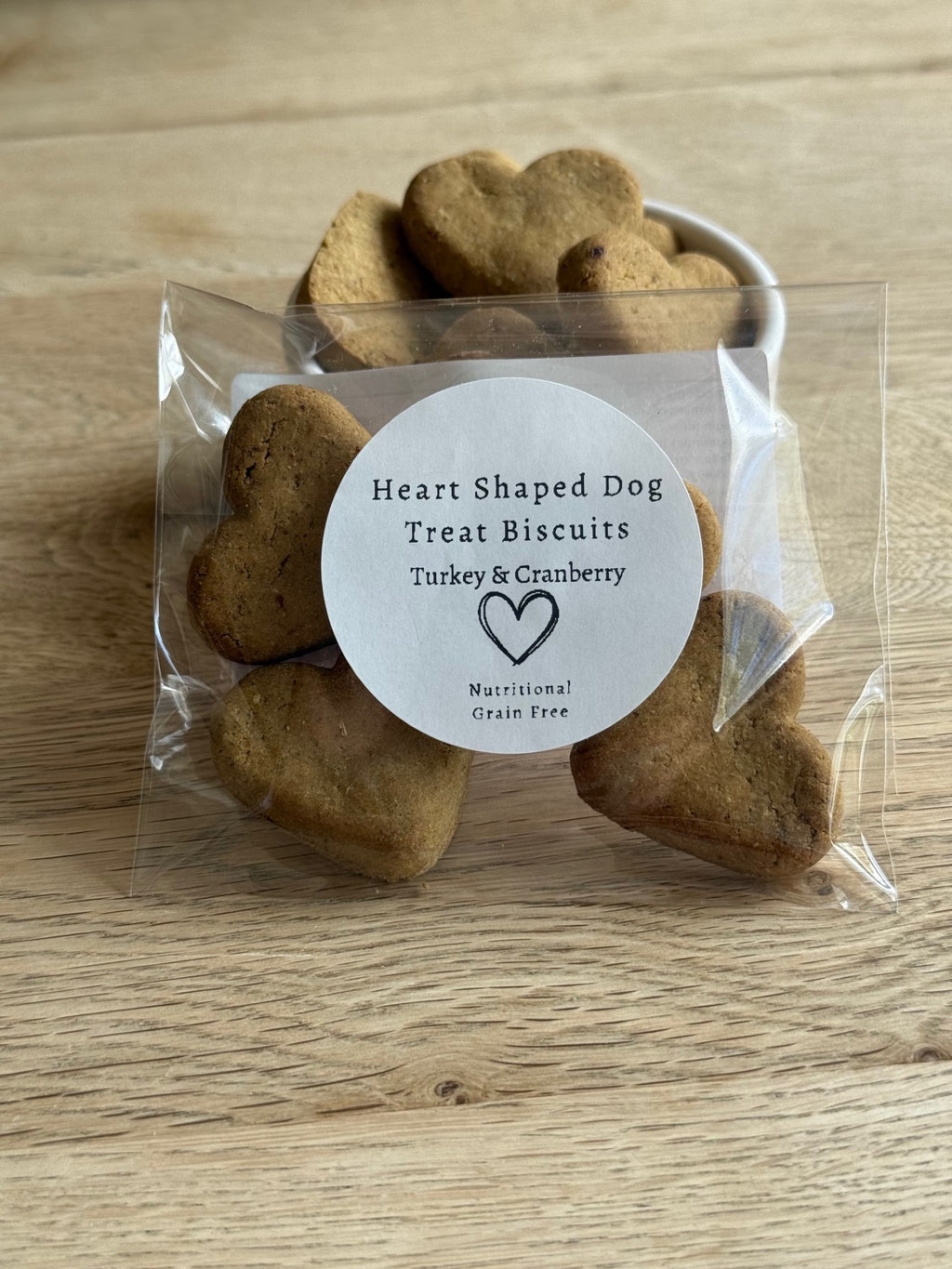 Heart-shaped dog treat biscuits in a clear package on a wooden surface